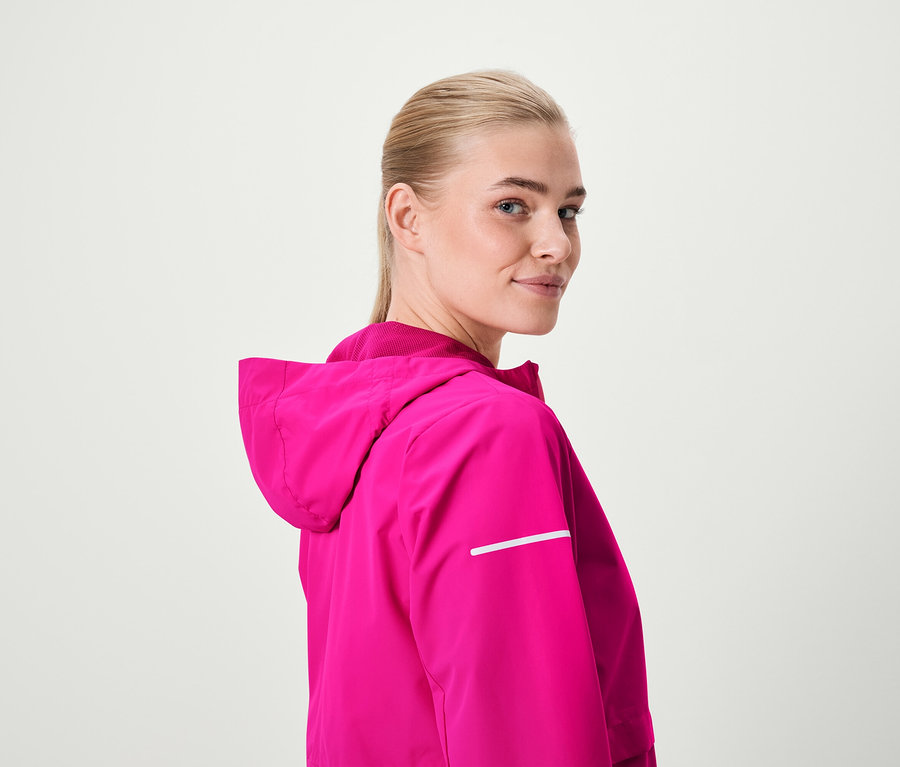 Blonde regardant par-dessus son épaule portant une veste à capuche rose.
