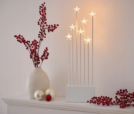 Décoration sur une commode blanche : vase avec des baies rouges, deux boules blanches et une rouge, un chandelier étoile blanc et une branche avec des baies rouges.