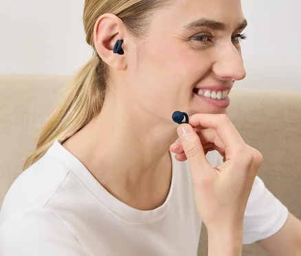 Une femme met un écouteur sans fil bleu foncé dans son oreille.