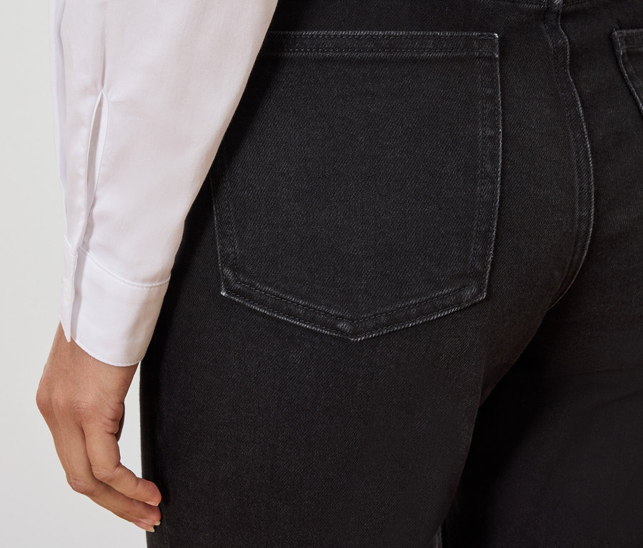 Vue détaillée de l'arrière d'un jean noir sur une personne portant une chemise blanche.