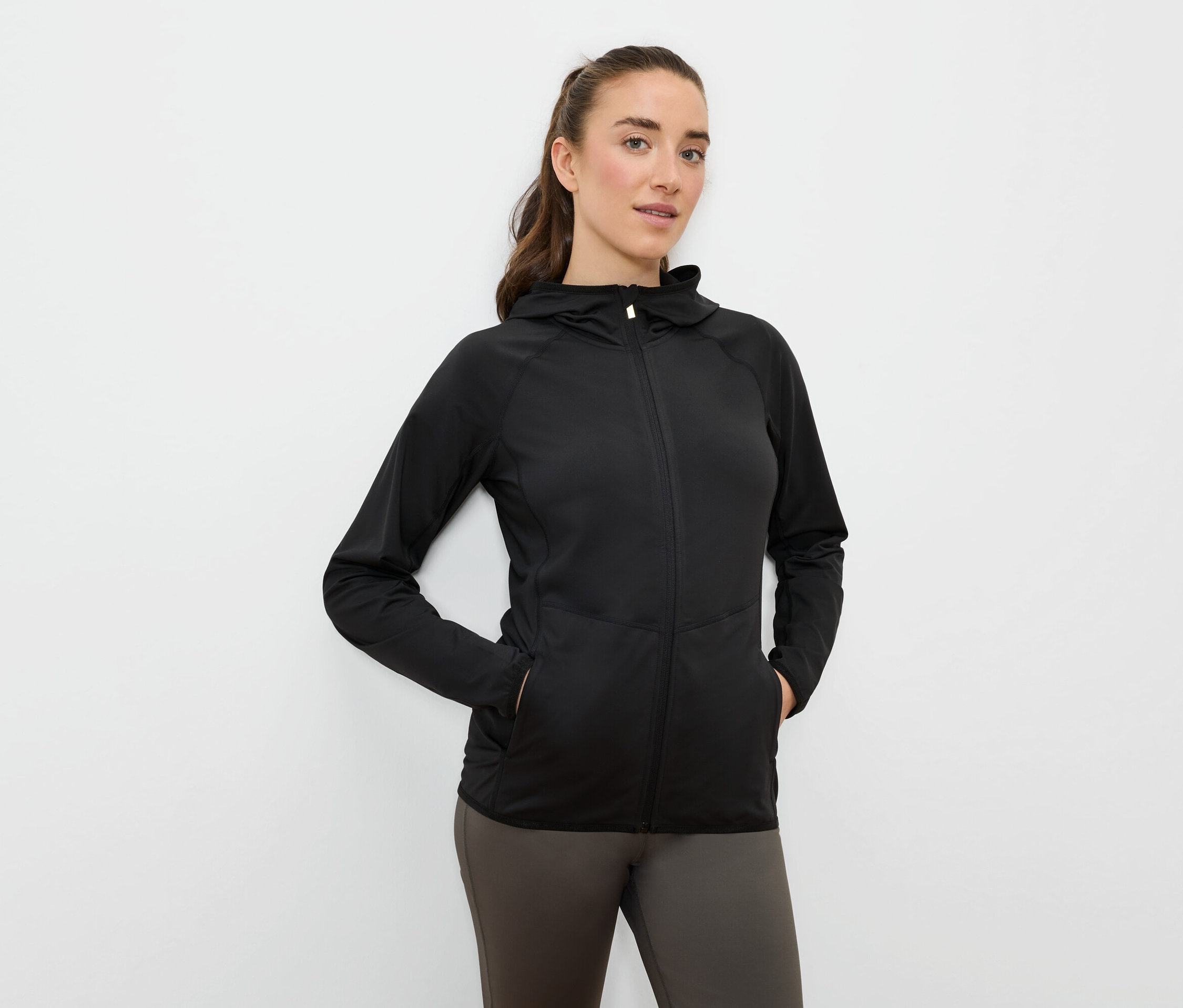 Une femme a les mains dans les poches d'une veste de sport noire à capuche et fermeture éclair.