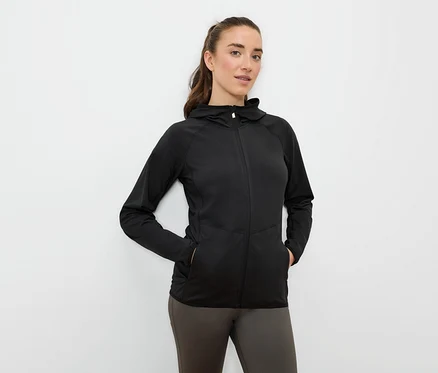 Une femme a les mains dans les poches d'une veste de sport noire à capuche et fermeture éclair.