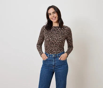 Femme brune posant dans un haut imprimé animalier et un jean bleu.