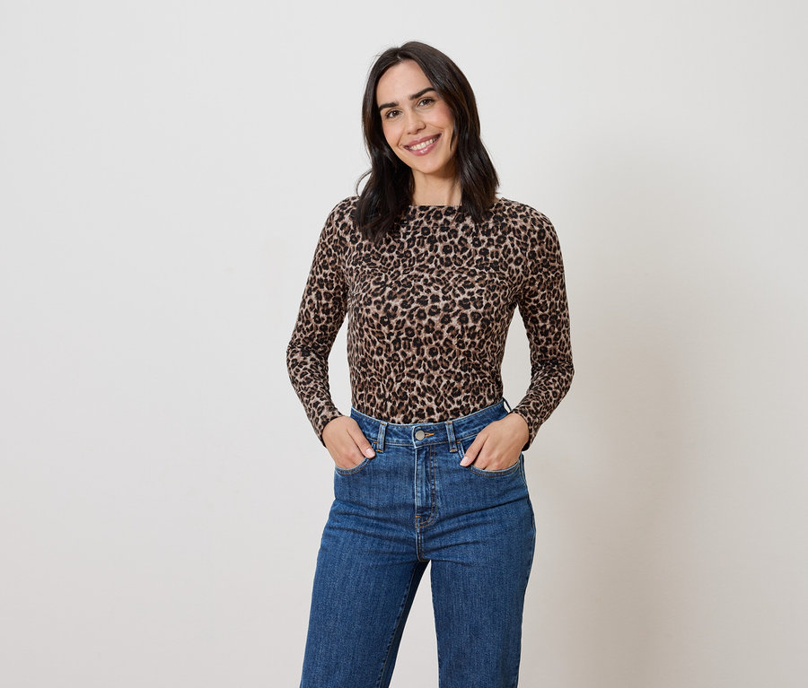 Femme brune posant dans un haut imprimé animalier et un jean bleu.