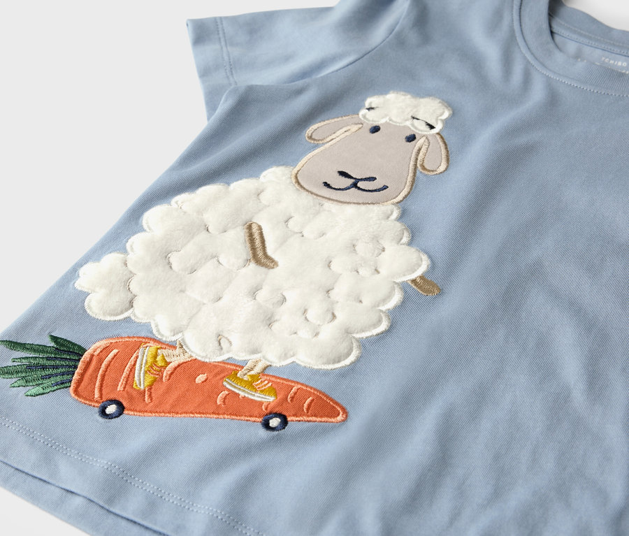 T-shirt bleu clair avec un appliqué de mouton sur une carotte à roulettes.