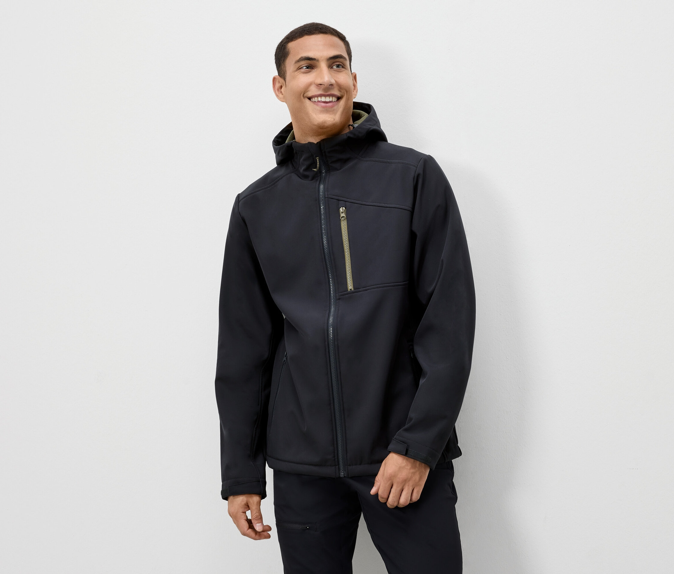 Un homme sourit et porte une veste noire à capuche.