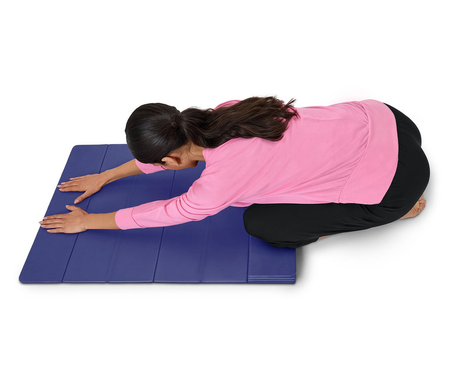 Femme en haut rose et pantalon noir s'étirant sur un tapis bleu.