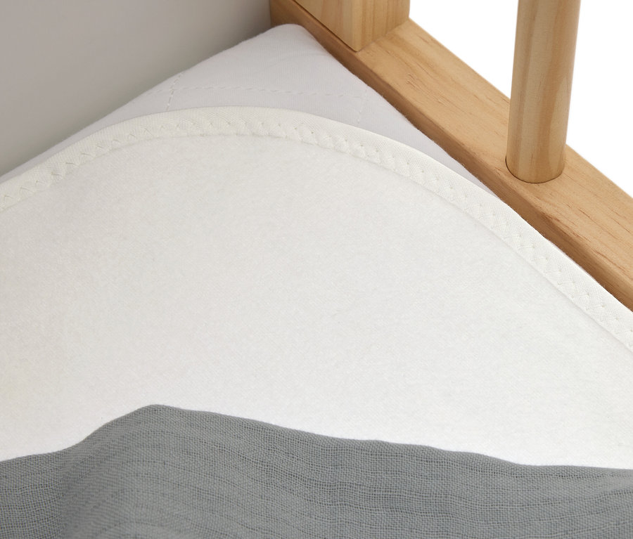 Gros plan d'un matelas blanc avec un tissu gris sur un lit en bois.