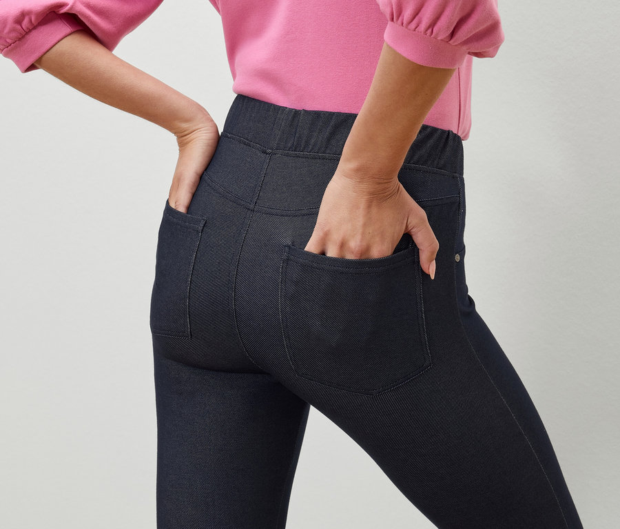 Une femme a sa main dans la poche de ses jeggings bleu foncé.