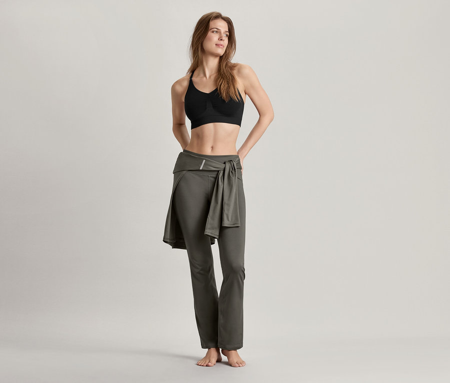 Femme portant un bustier de sport sans coutures, noir et un pantalon de sport modelant, vert olive.