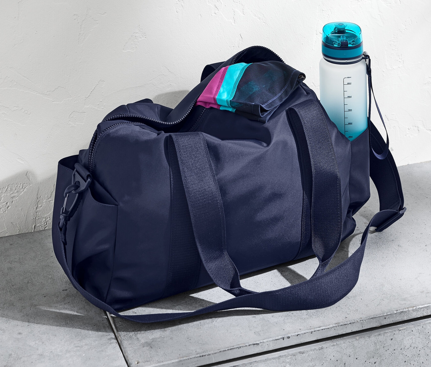 Un sac de sport bleu marine et une bouteille d'eau sur une surface en béton.