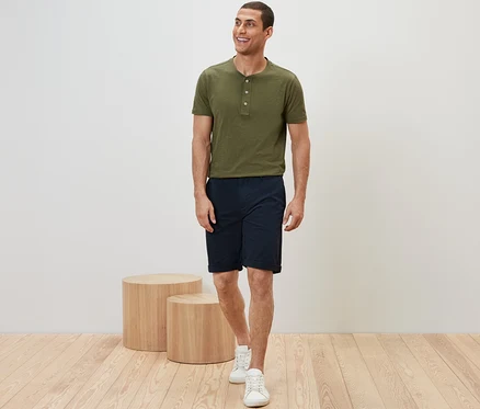 Un homme portant un t-shirt kaki et un short chino bleu marine, marchant.