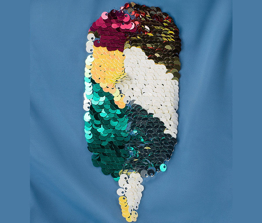 Gros plan d'un maillot de bain pour enfant avec des paillettes réversibles en forme de goutte, disposées en blocs de couleur.