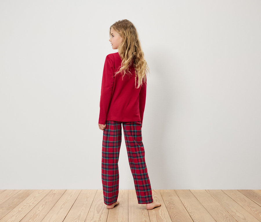 Une fille en pyjama rouge avec un pantalon à carreaux se tient dos au spectateur.