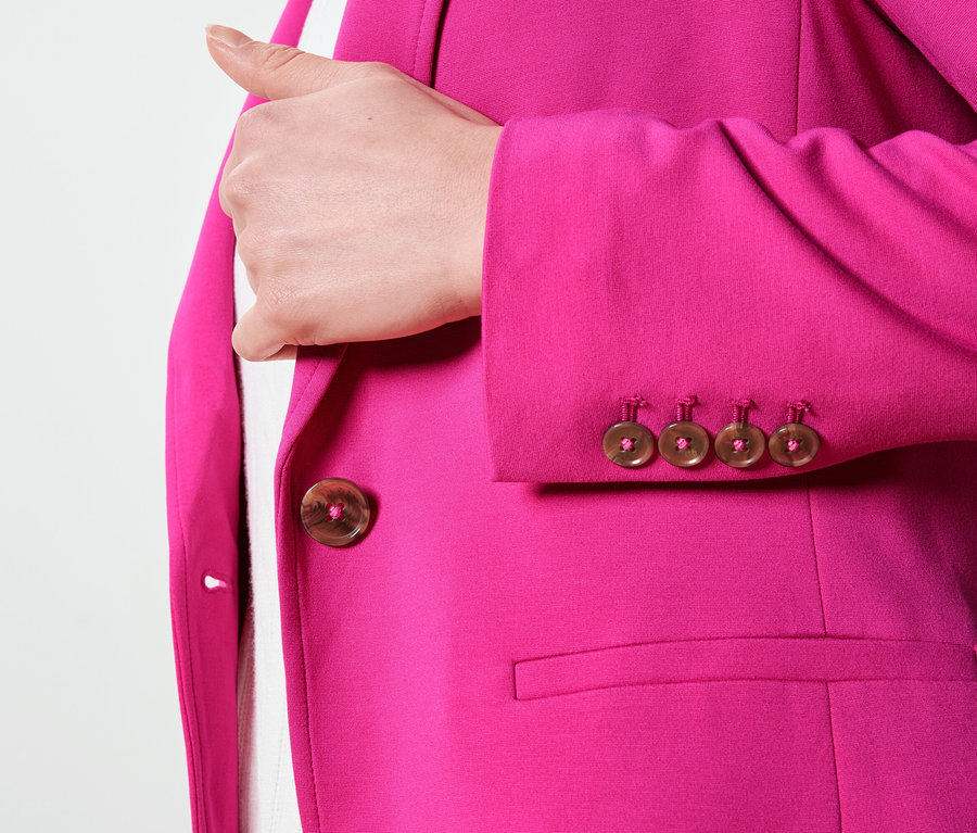 Gros plan sur un blazer rose avec des boutons marron sur les manches et la fermeture.