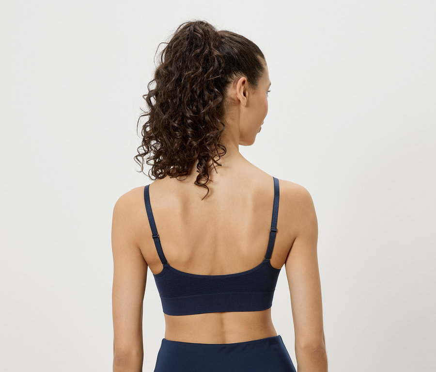 Vue de dos d'une femme aux cheveux bouclés portant un soutien-gorge de sport bleu marine.