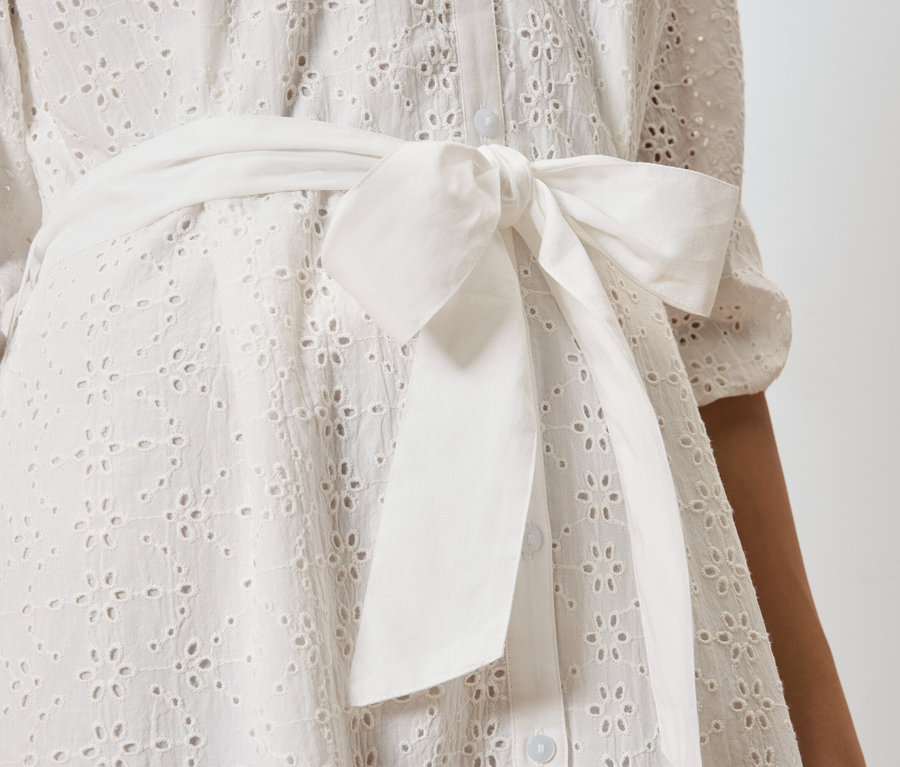 Gros plan sur une robe blanche en broderie anglaise avec un nœud à la taille.