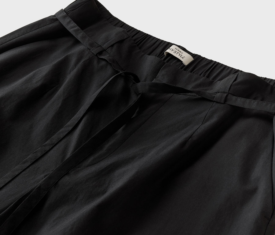 Gros plan sur un pantalon noir avec une ceinture à nouer et une étiquette portant l'inscription "TCHINO MY STYLE".