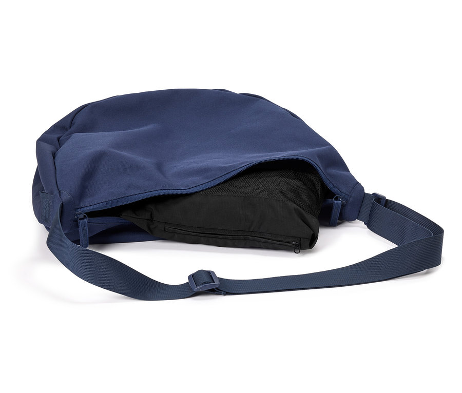 Sac bandoulière bleu marine avec un contenu noir et une bandoulière réglable posé sur un fond blanc.