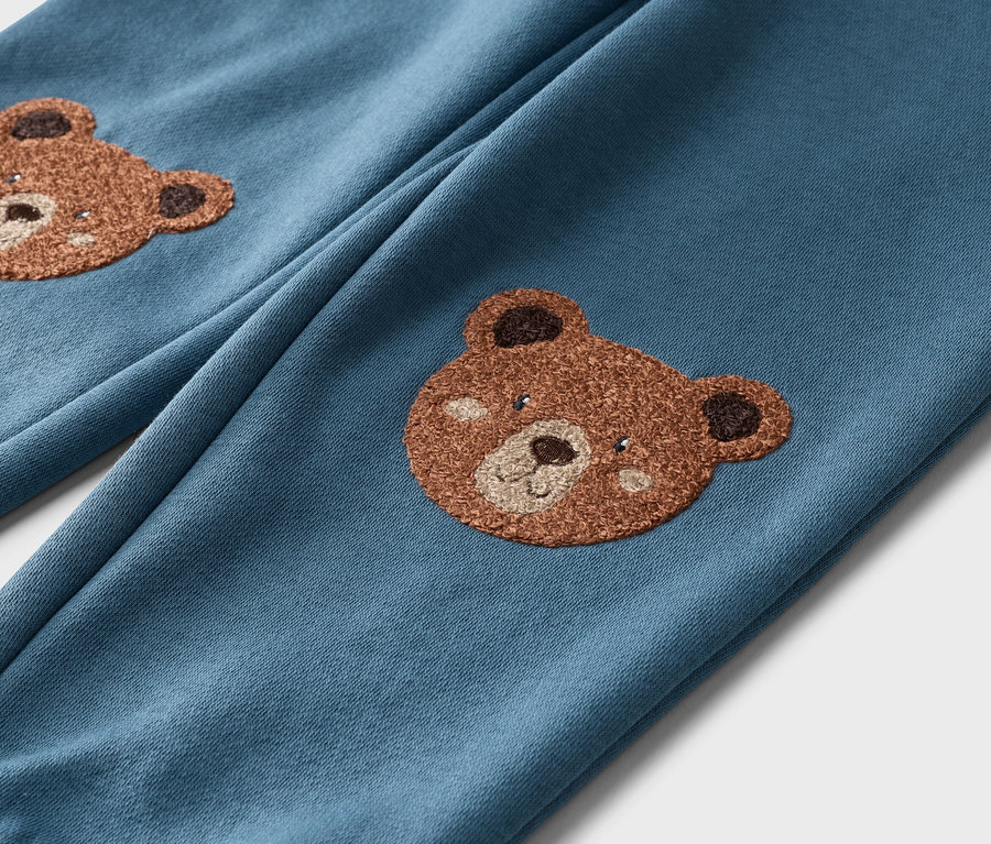 Gros plan d'un pantalon bleu avec des appliqués d'ours en peluche sur les deux jambes.