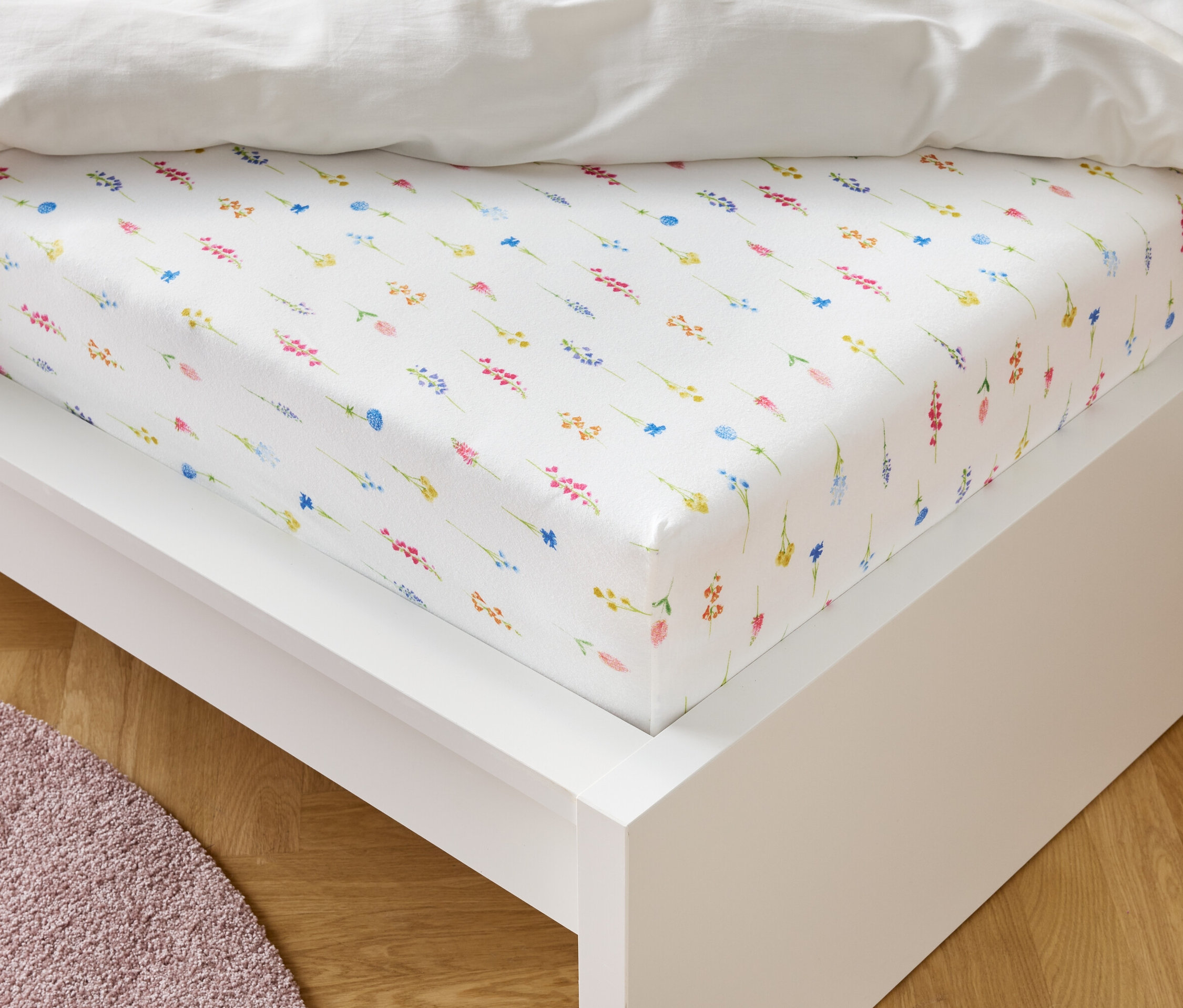 Un drap-housse blanc à motif floral est posé sur un cadre de lit blanc.