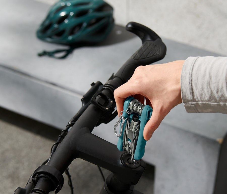 Une main fixe un outil multifonction sur le guidon d'un vélo, avec un casque de vélo en arrière-plan.