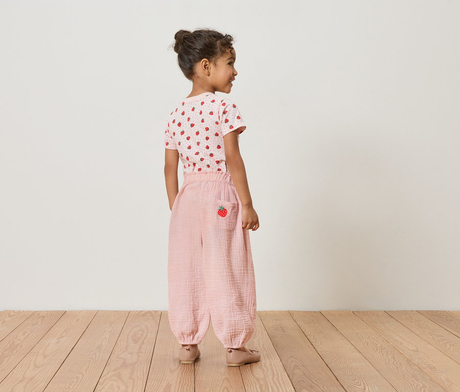 Fillette vue de dos, portant un t-shirt à fraises et un pantalon rose avec un détail fraise.