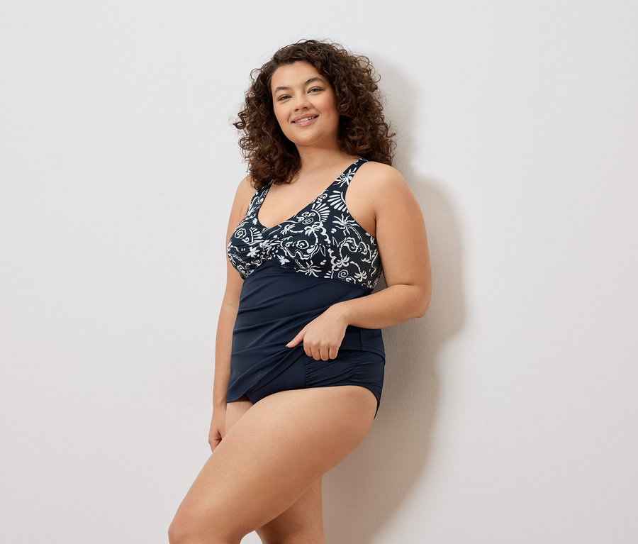 Une femme aux cheveux bouclés porte un maillot de bain bleu marine à imprimé floral.