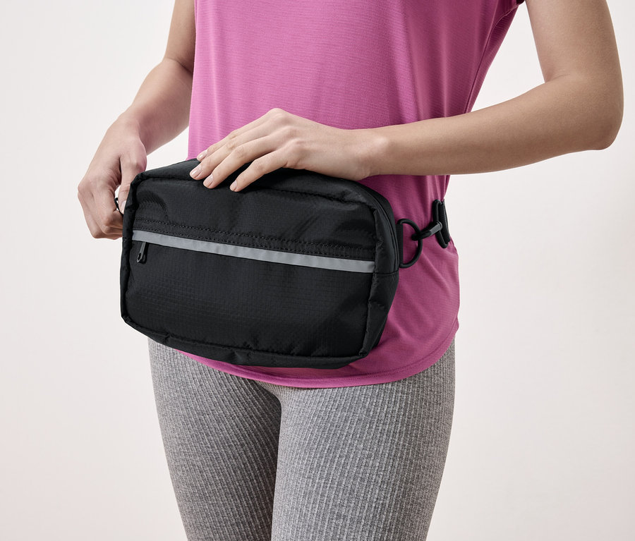 Une femme portant un sac banane noir avec une bande réfléchissante.