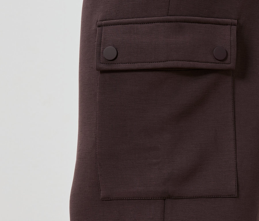 Vue détaillée d'un pantalon châtaigne avec une poche plaquée fermée par deux boutons ronds.