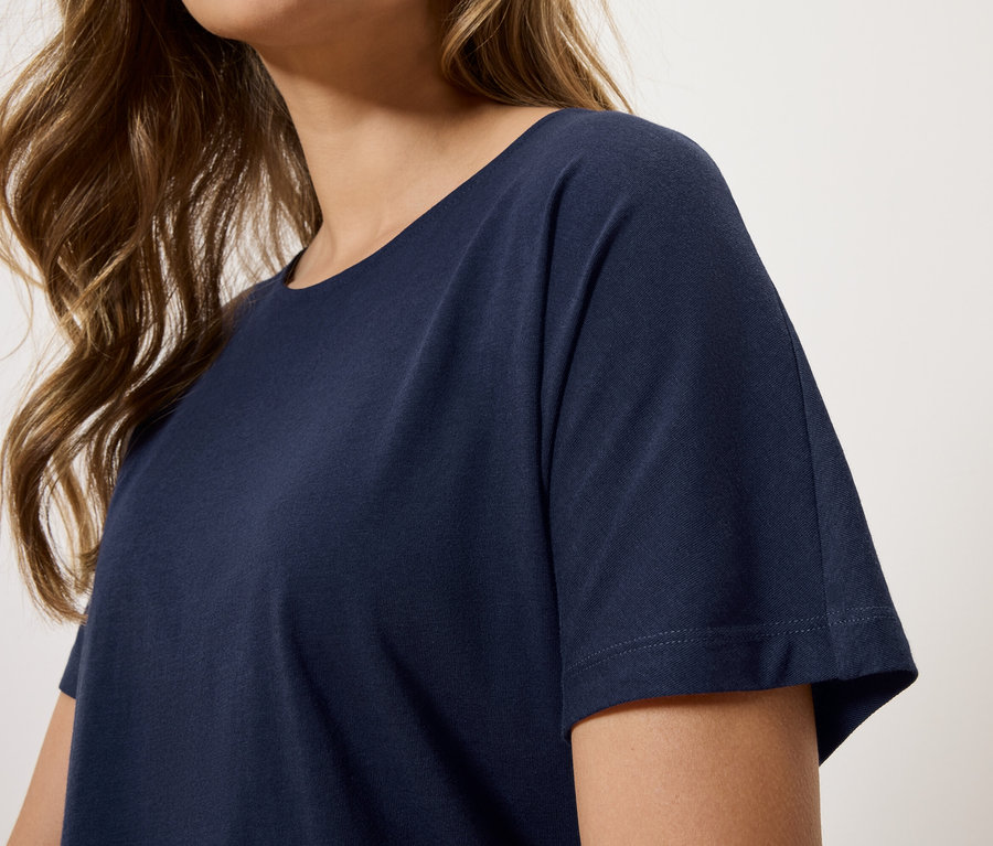Gros plan d'une femme aux cheveux bruns ondulés portant un t-shirt bleu marine.