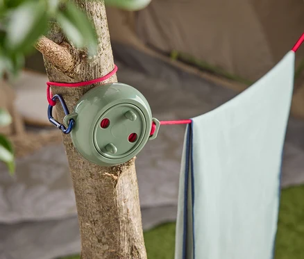 Un étendoir à linge vert avec un mousqueton bleu est attaché à un arbre, avec une serviette bleu clair suspendue.