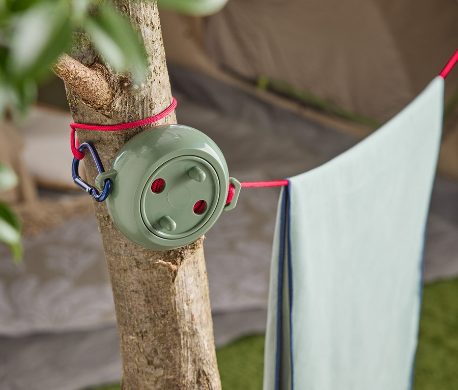 Un étendoir à linge vert avec un mousqueton bleu est attaché à un arbre, avec une serviette bleu clair suspendue.