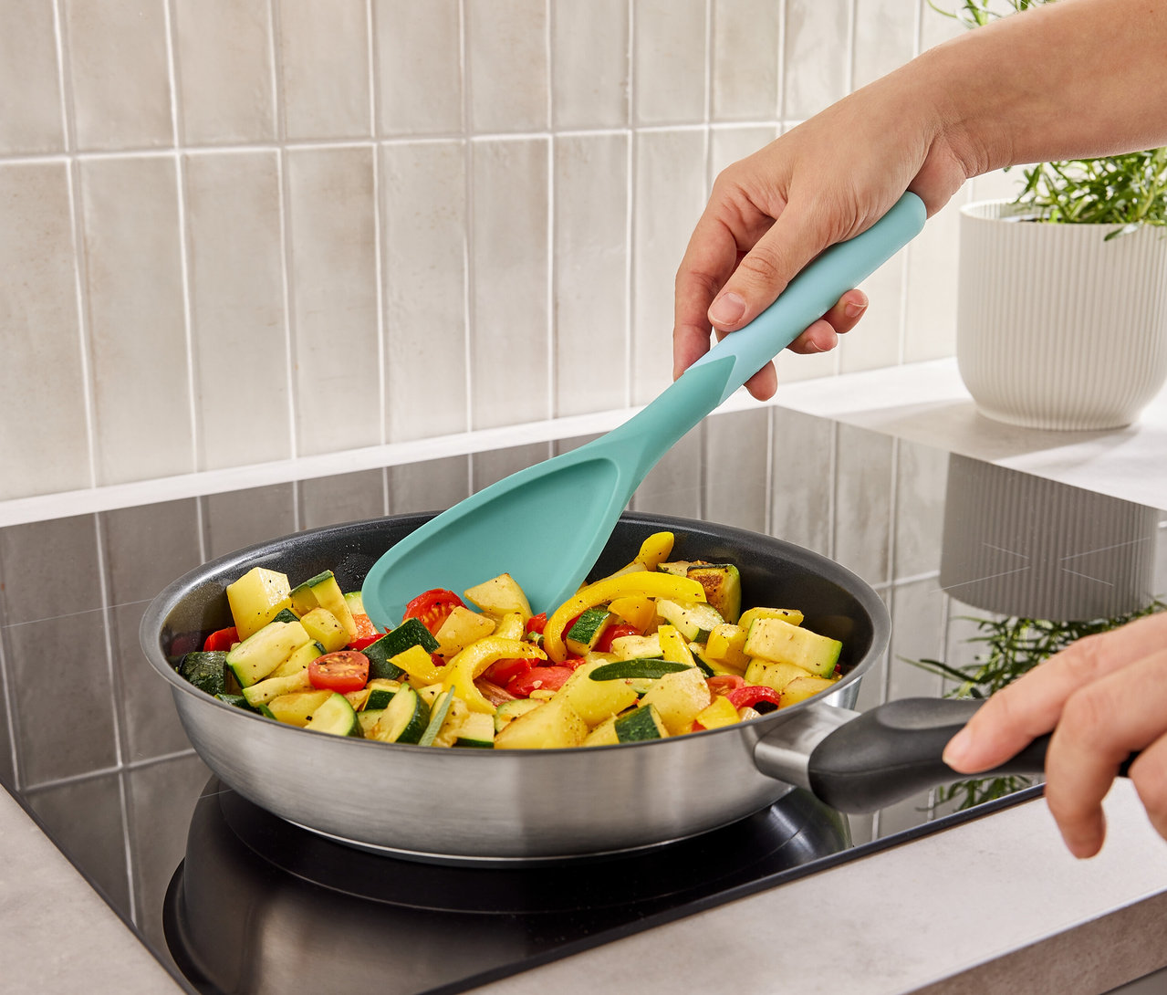 Une personne mélange des légumes dans une poêle sur une cuisinière avec un ustensile de cuisine turquoise.