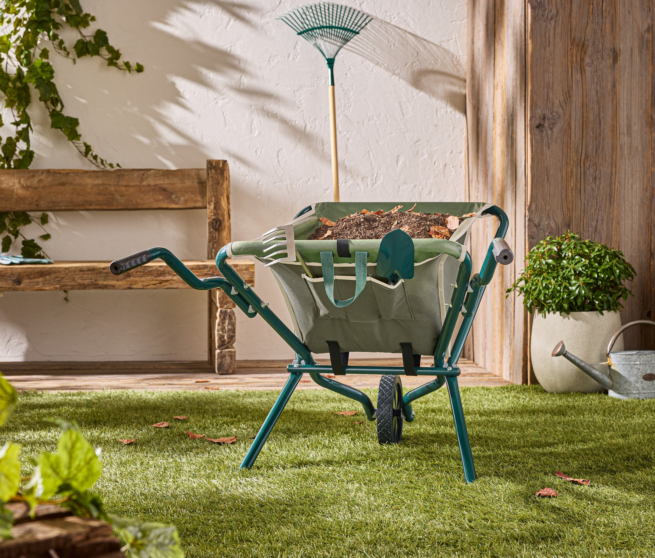 Une brouette verte se tient sur une pelouse avec des outils de jardinage à l'intérieur.