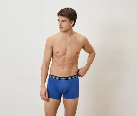 Homme torse nu portant un boxer bleu sur fond clair.