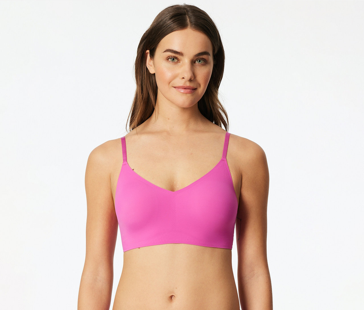 Une femme porte une brassière invisible SCHIESSER rose avec coussinets et sourit à la caméra.