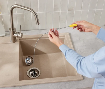 Une personne utilise un furet de plomberie pour nettoyer le drain d'un évier de cuisine.