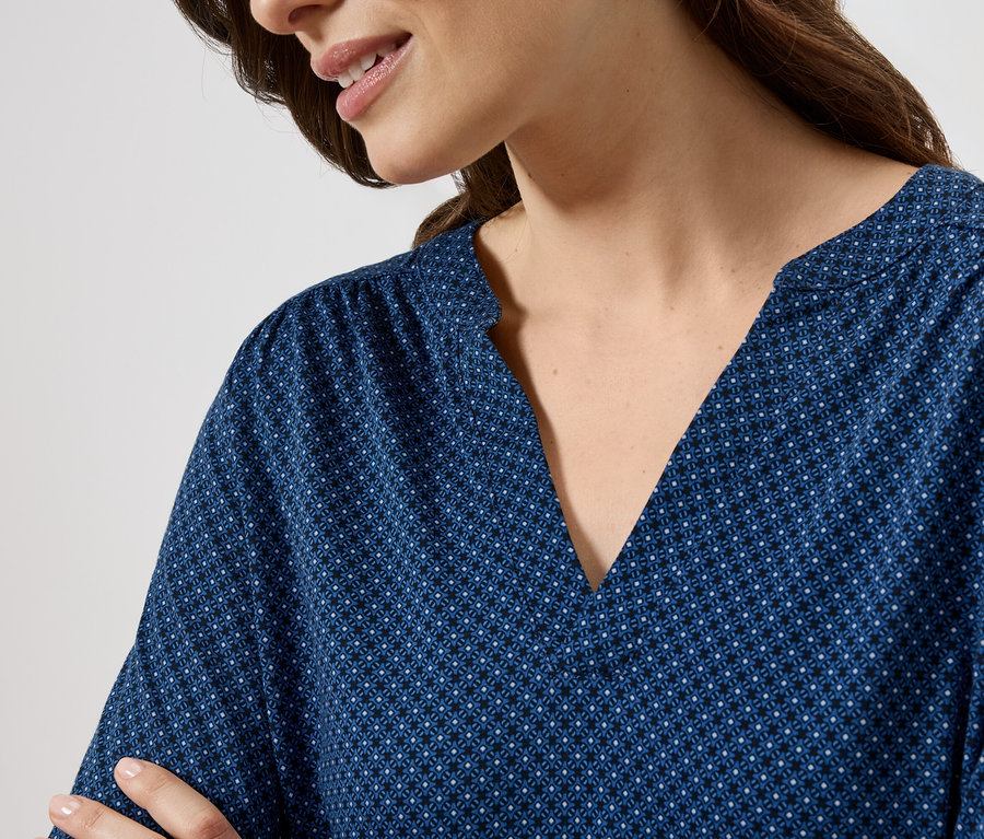 Femme portant un chemisier bleu à motifs avec un col en V.
