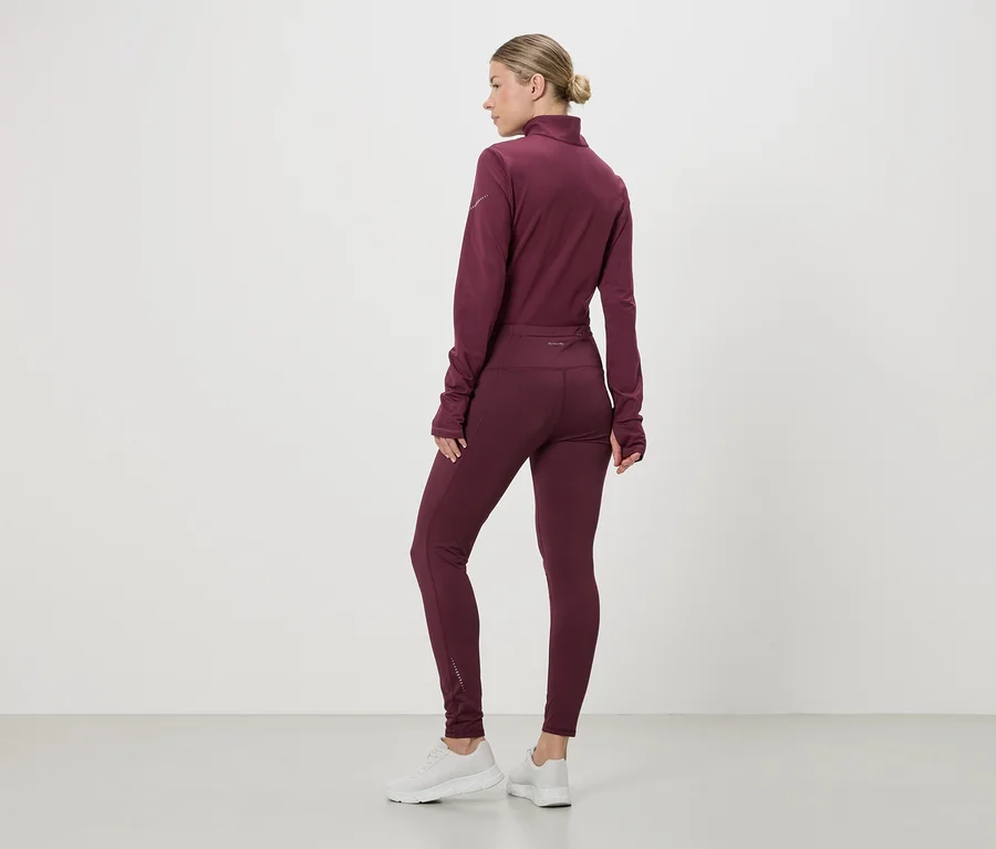 Femme vue de dos portant une tenue de sport bordeaux et des baskets blanches. Le haut a une fermeture éclair et des manches longues.