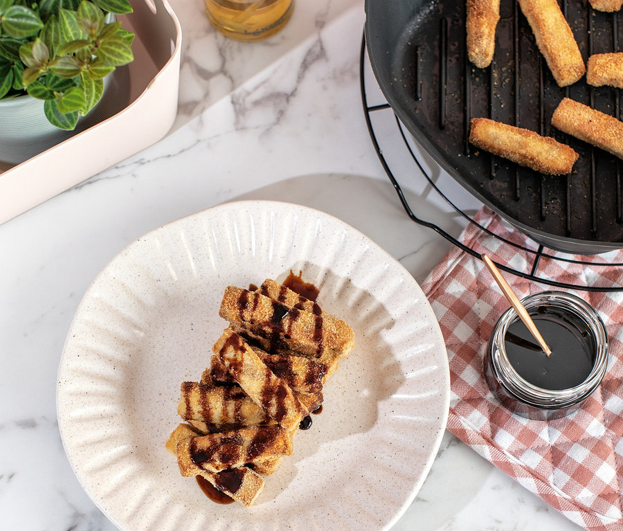 Sur une table en marbre, une assiette de bâtonnets de pâte garnis, une poêle à griller avec des bâtonnets de pâte et une bouteille d'huile.
