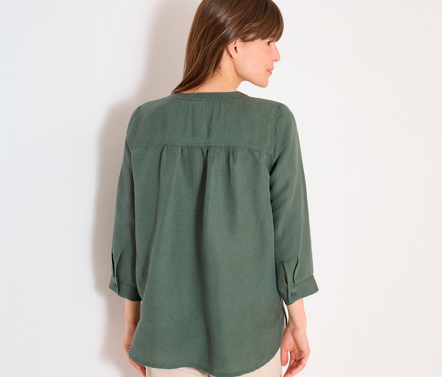 Femme vue de dos portant un chemisier vert olive à manches trois-quarts et un pantalon beige sur fond blanc.