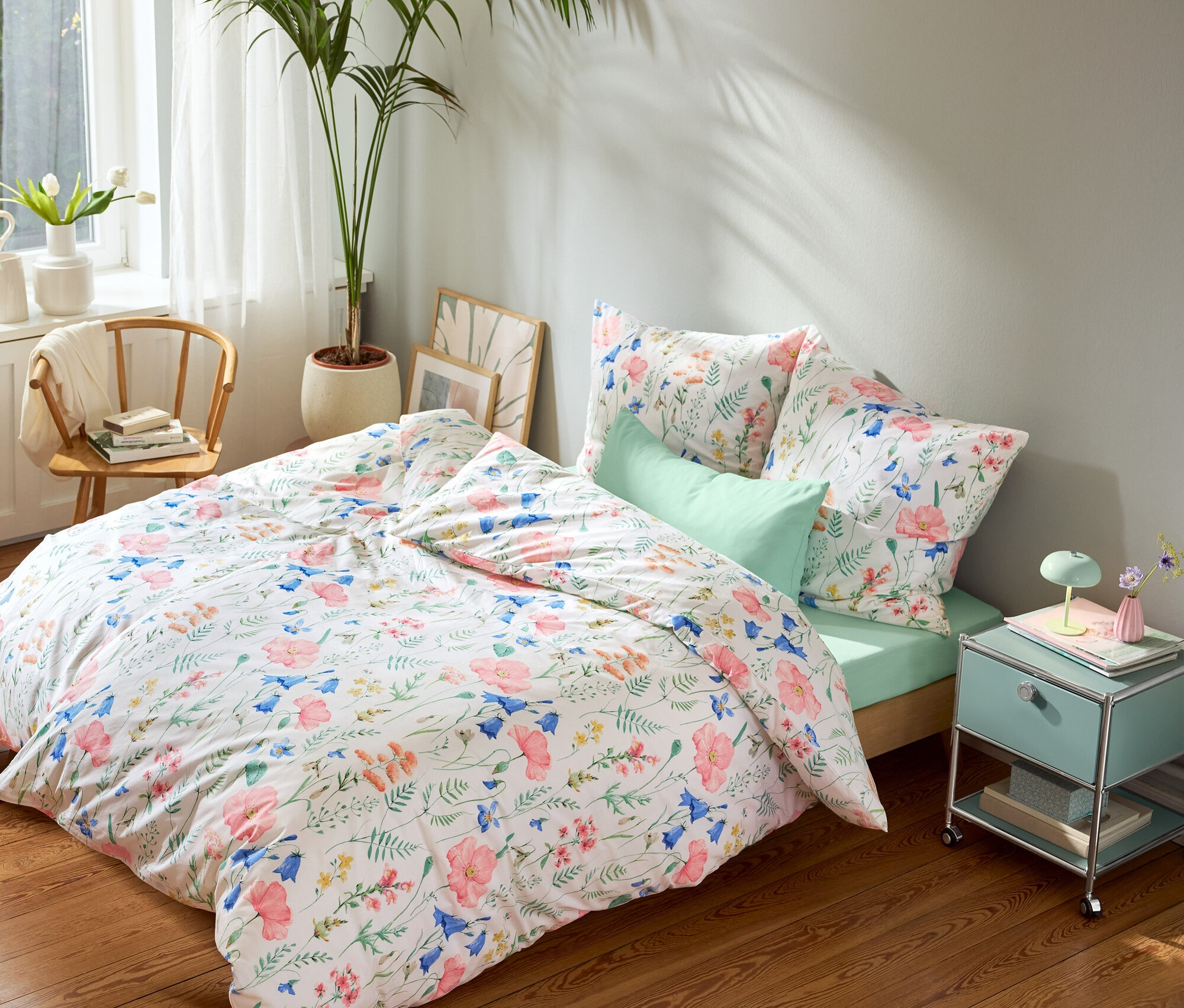 Lit avec des draps à motifs floraux, un drap-housse vert menthe et des taies d'oreiller vert menthe, une table de chevet vert menthe et un tapis rond.