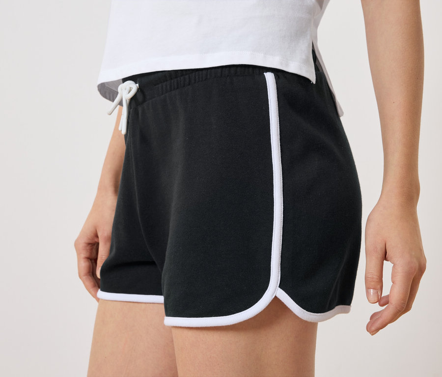 Gros plan d'une femme portant un short noir avec des rayures latérales blanches et un cordon de serrage blanc.