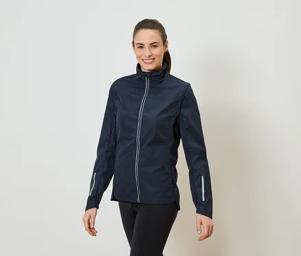 Une femme avec une queue de cheval porte une veste bleu marine zippée et un legging noir.