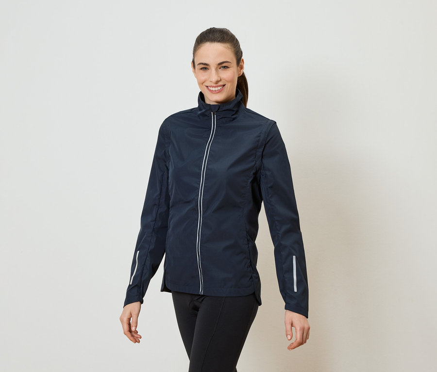 Une femme avec une queue de cheval porte une veste bleu marine zippée et un legging noir.