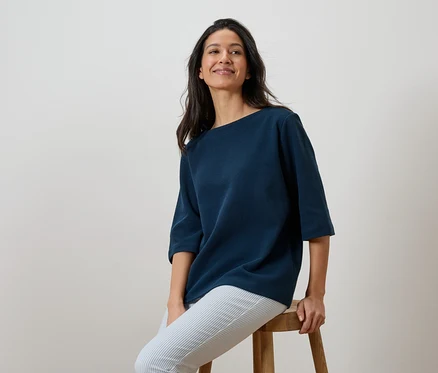 Femme assise sur un tabouret, portant un t-shirt bleu marine et un pantalon rayé.