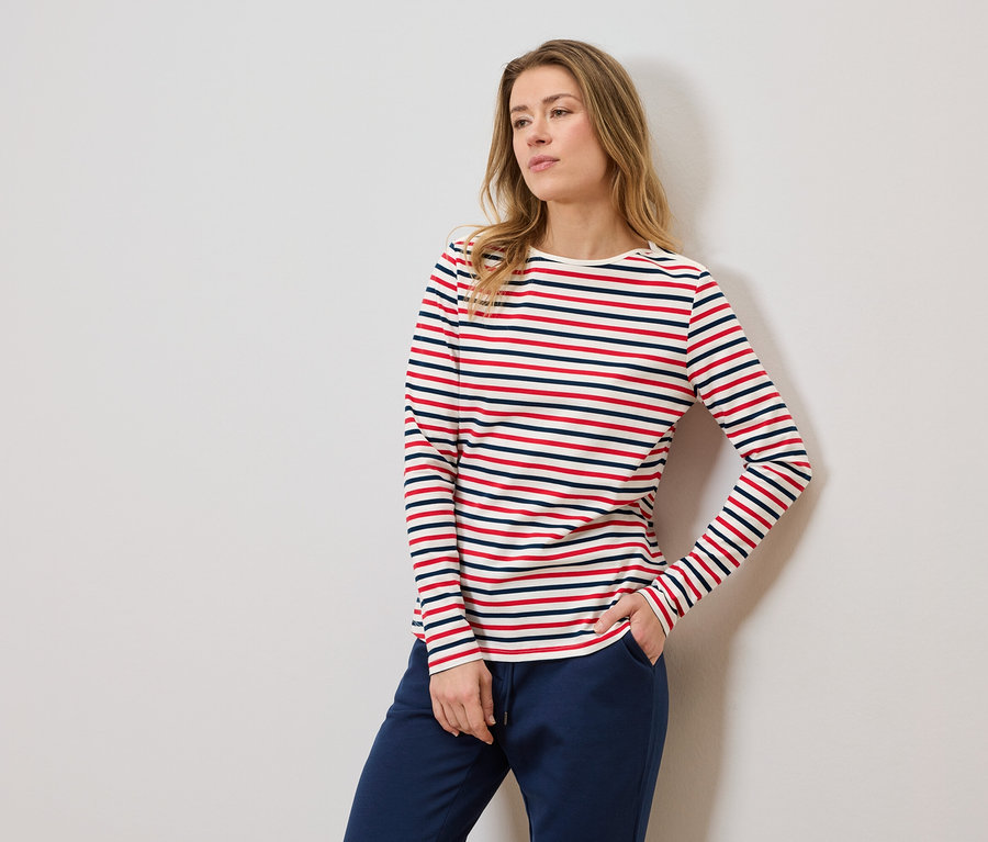 Femme portant un t-shirt rayé à manches longues et un pantalon de jogging bleu, une main dans la poche.
