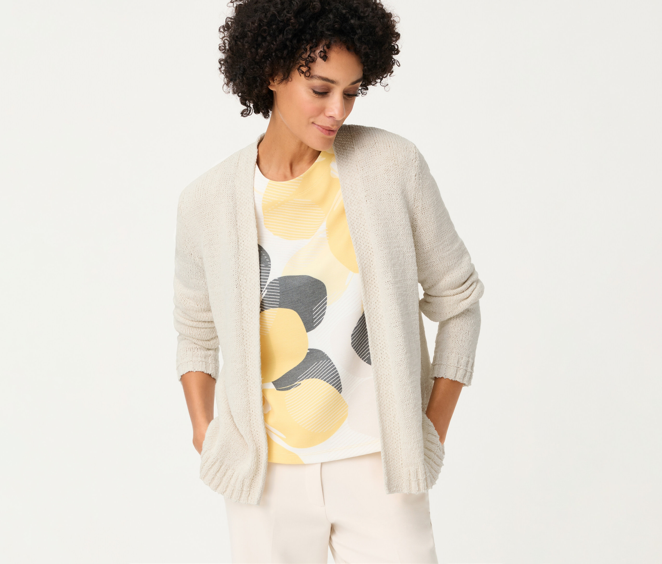 Femme portant un cardigan en lin Olsen sur un t-shirt à cercles jaunes et gris, les mains dans les poches.