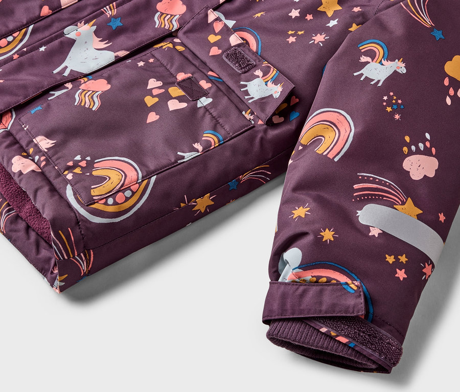 Gros plan sur une veste violette à motifs de licornes, d'arcs-en-ciel et d'étoiles, montrant des poches et une manche.